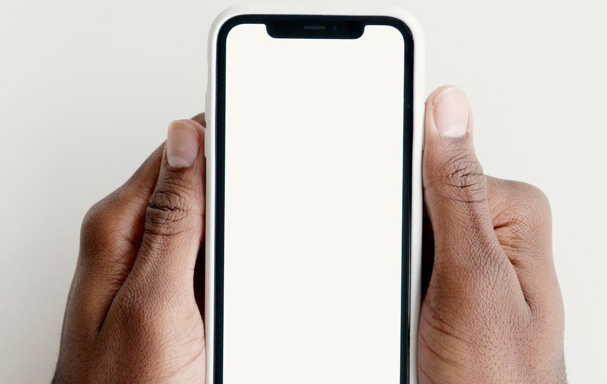 Mãos segurando um celular com a tela em branco sobre uma mesa