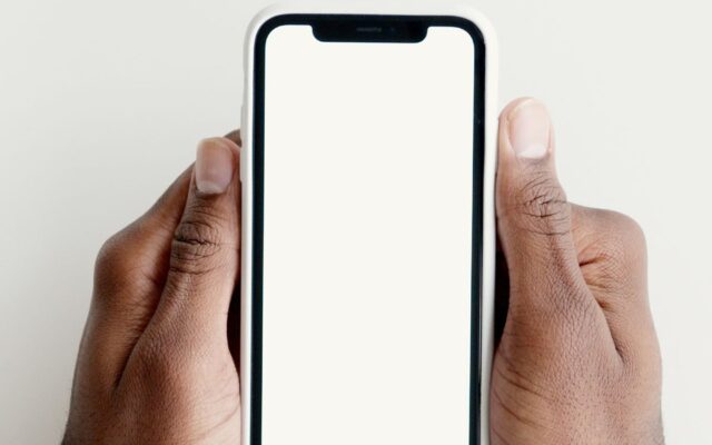 Mãos segurando um celular com a tela em branco sobre uma mesa