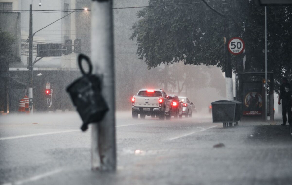 Chuva intensa sobre uma rua urbana com carros e pavimento molhado