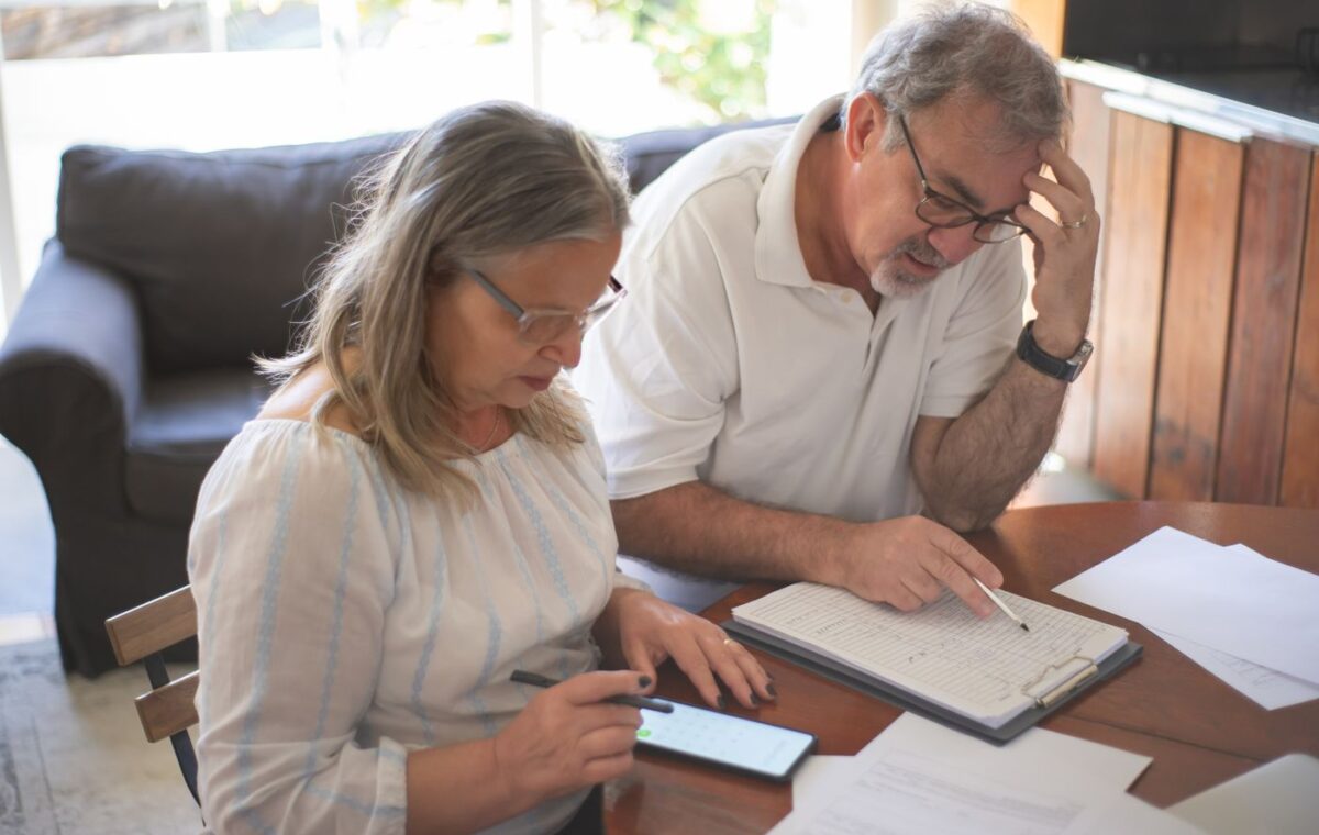 Casal idoso consulta documentos financeiros e um smartphone à mesa