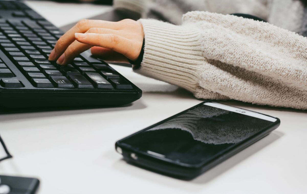 Mão digita em teclado ao lado de um telefone celular