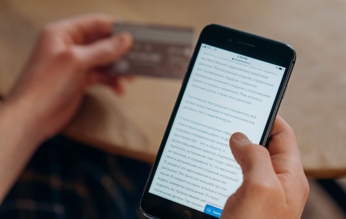 Pessoa consulta um smartphone enquanto segura um cartão bancário