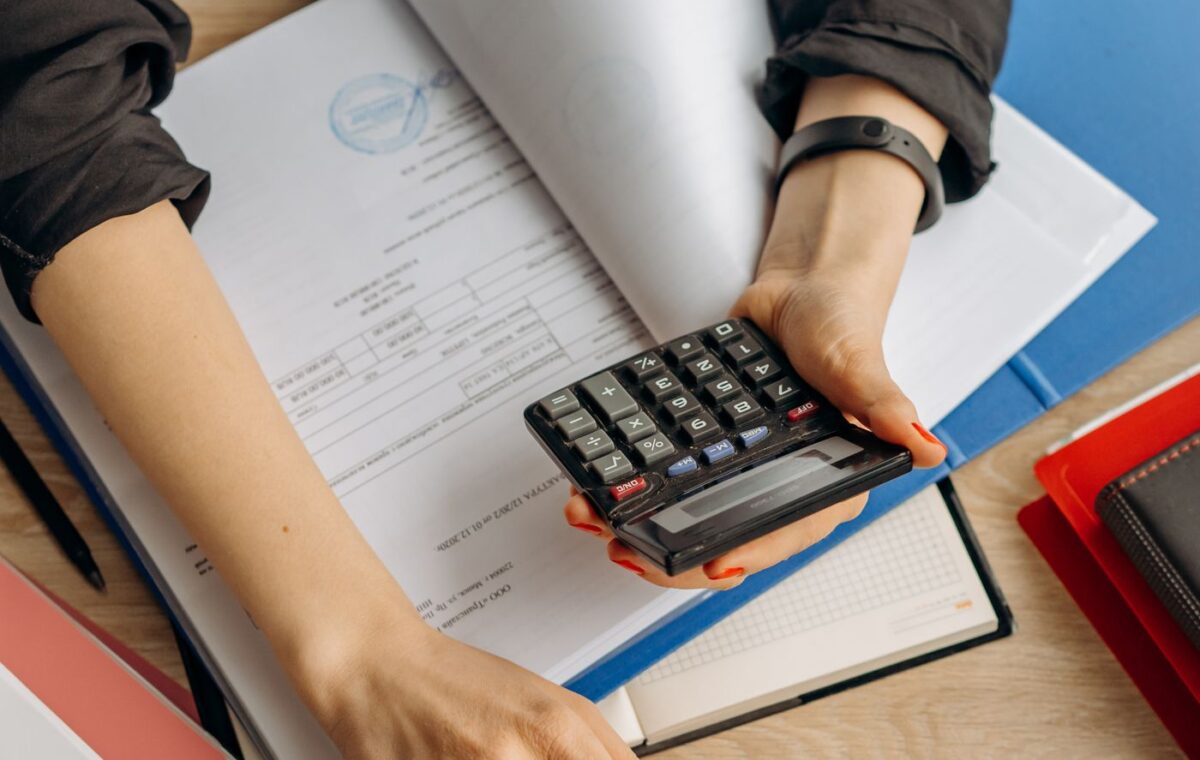 Pessoa usa calculadora ao lado de computador portátil e documentos