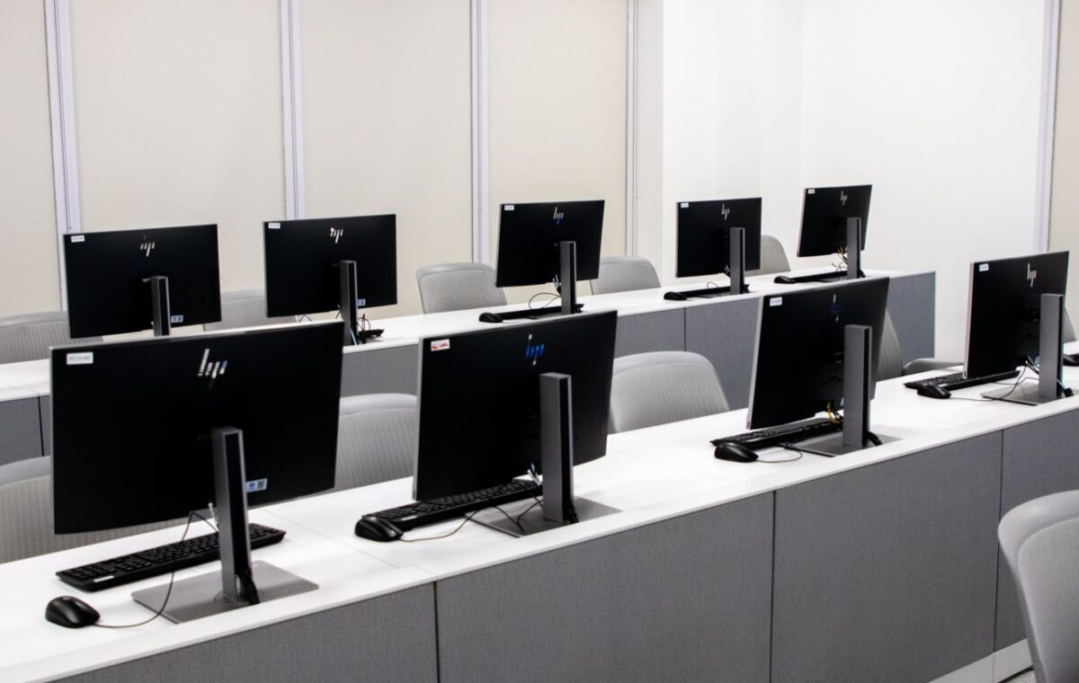 Sala de informática vazia com fileiras de computadores e cadeiras