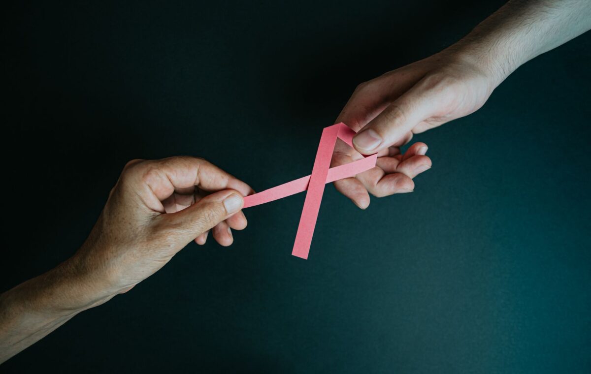 Duas mãos seguram laço rosa de conscientização sobre câncer de mama