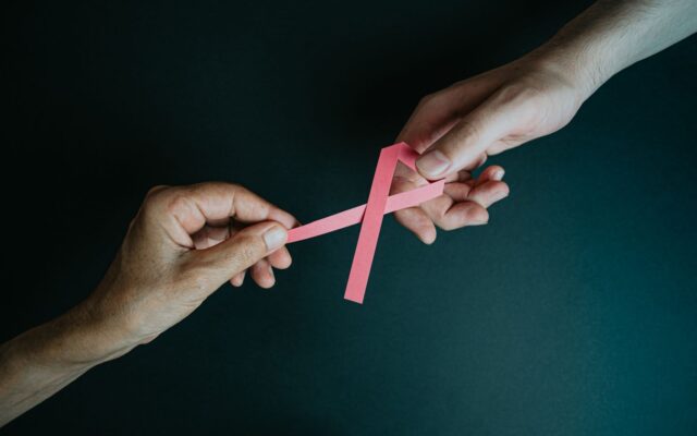 Duas mãos seguram laço rosa de conscientização sobre câncer de mama