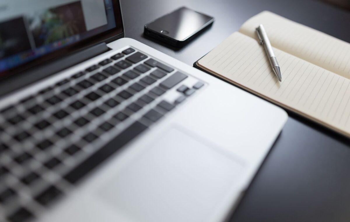 Computador portátil, caderno, celular e caneta sobre uma mesa