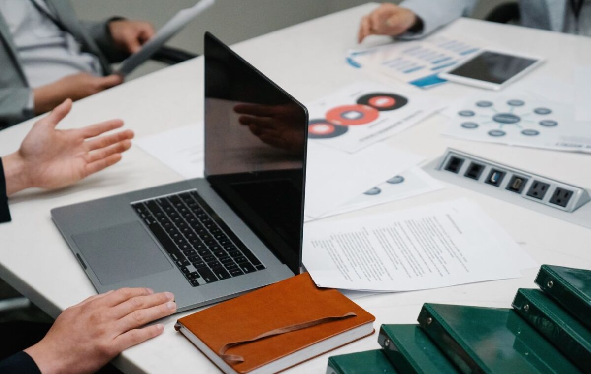 Mesa de reunião com notebook e documentos durante uma conversa de trabalho