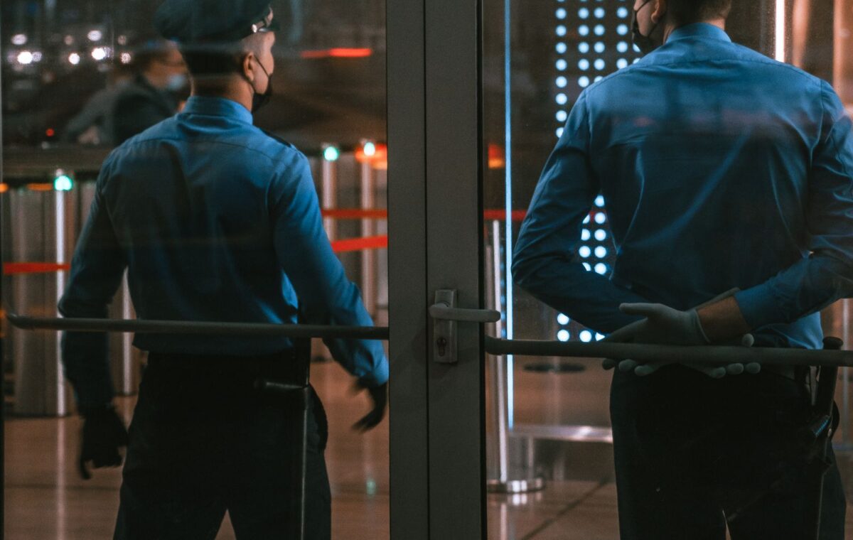 Dois vigilantes diante da entrada envidraçada de um edifício